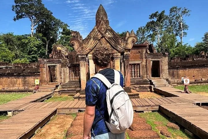 A tourist with a backpack standing before a stone temple gate structure.