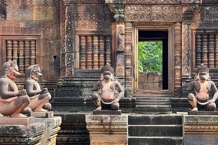 Estatuas de figuras arrodilladas que custodian la entrada de un templo de piedra lleno de detalles.